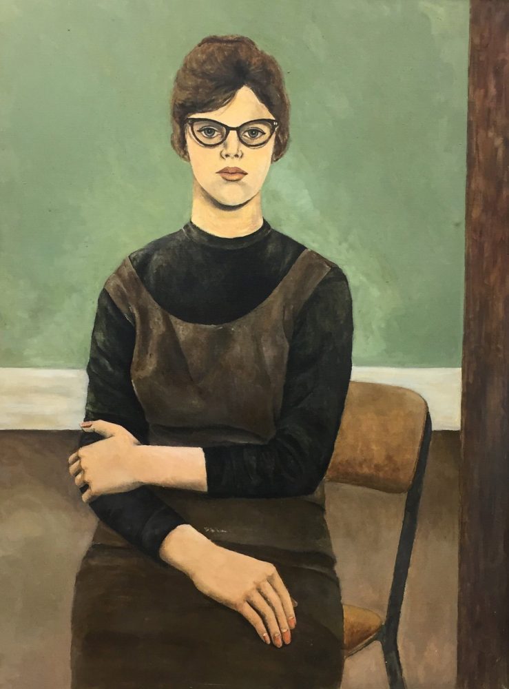 A woman wearing a dark grey dress over a black turtleneck sits on a low chair in the center of a painting. She looks out at the viewer directly with a relaxed expression wearing black cat-eye glasses. Her brown hair is tied up, and one of her arms hangs casually in front of her body, while the other reaches up to hold it at the elbow. The wall behind her is divided in half horizontally by a white band, with the top half of the wall painted a pale green and the bottom painted brown.
