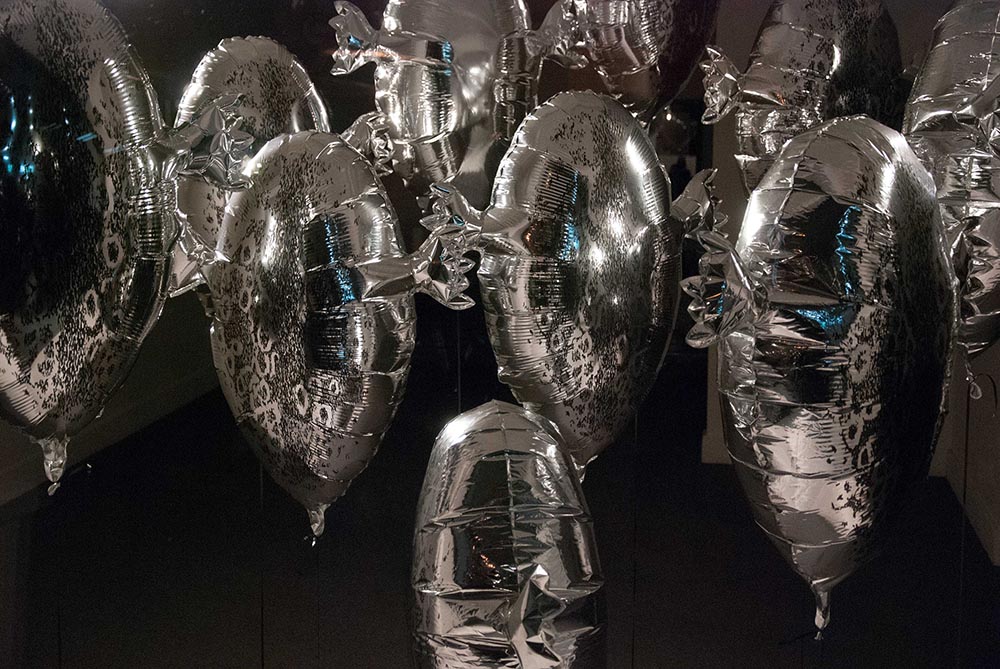 Shiny silver foil balloons shaped like seal skin floats, and printed with a fur pattern are lit by spotlights as they appear suspended in a darkened space.