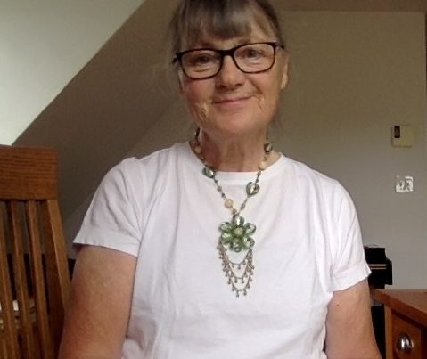Portrait of Owens Art Gallery Director Emerita Gemey Kelly seated wearing black-rimmed glasses, a white top and intricate green necklace.