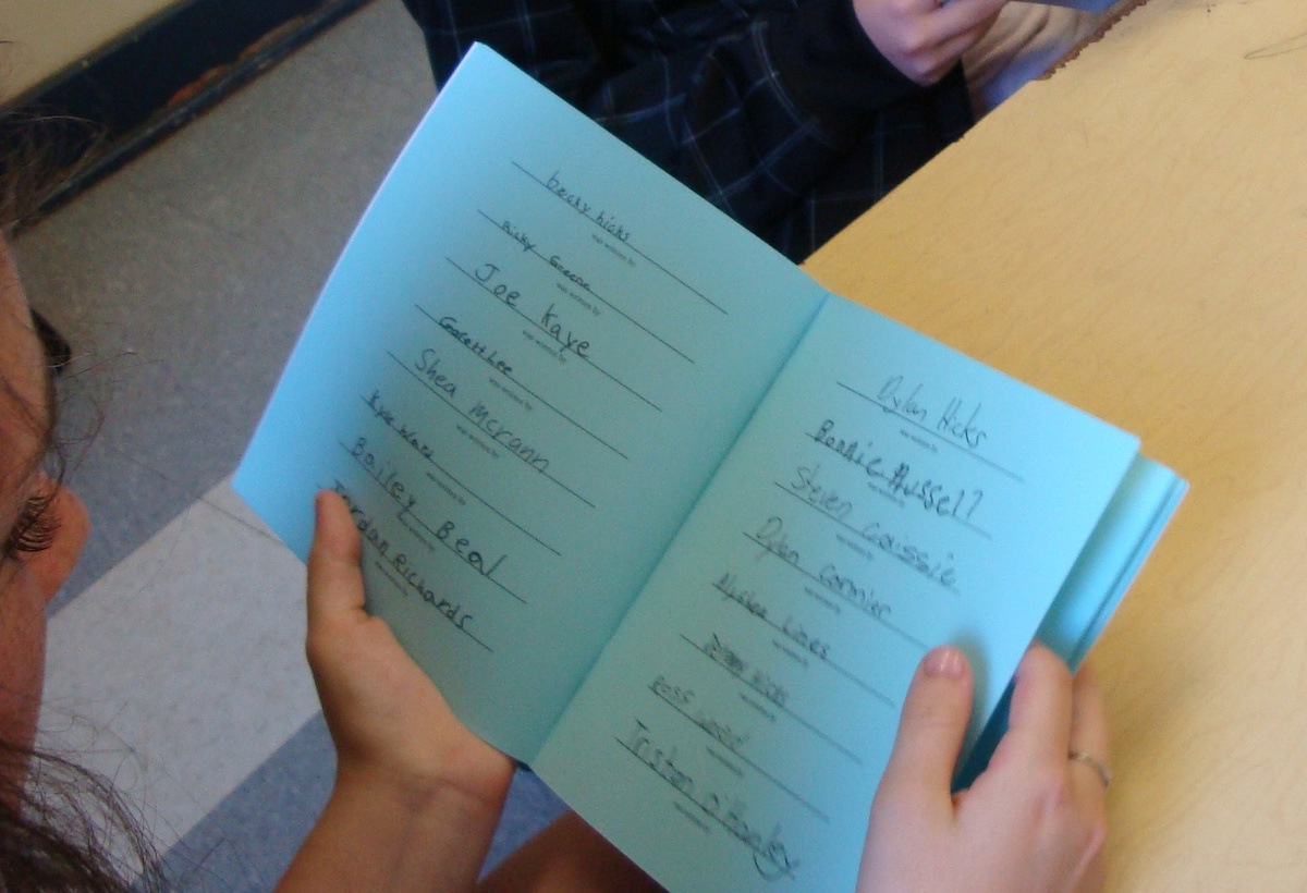 A young person looks at a book with blue pages. The facing pages each contain a list of handwritten names.