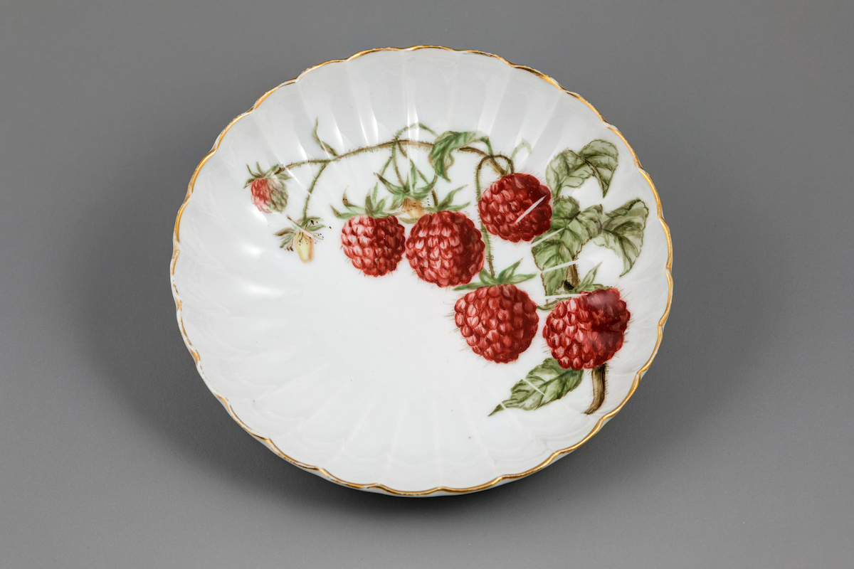 A dessert plate with gilded scolloped edges and a raspberry motif.