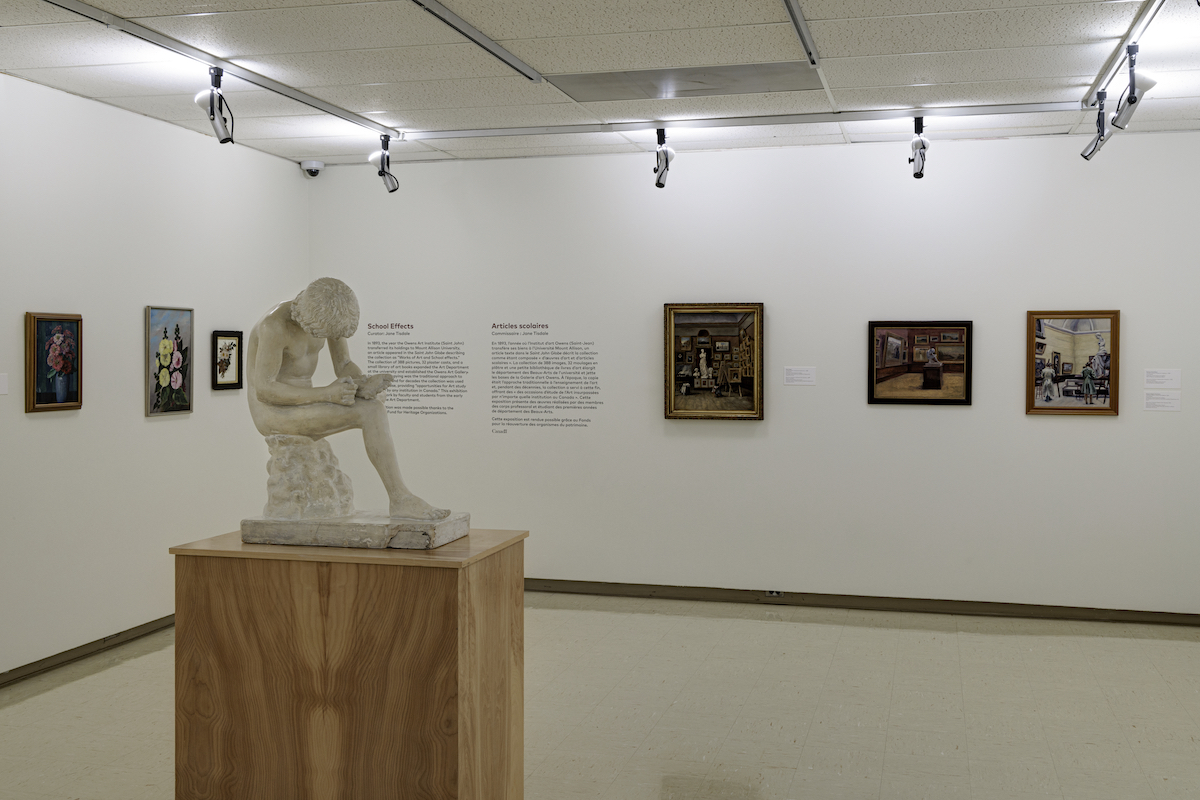 A plaster sculpture of a boy removing a thorn from his foot is on display in the centre of a gallery. Six paintings hang on the walls behind the sculpture.