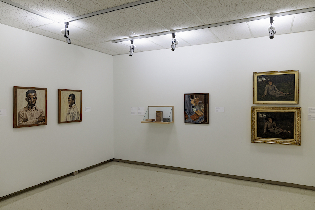 Five paintings and a display case hang in a white walled gallery. Two pairs of paintings show the same subject, one a man with dark skin and the other a woman seated in a field.