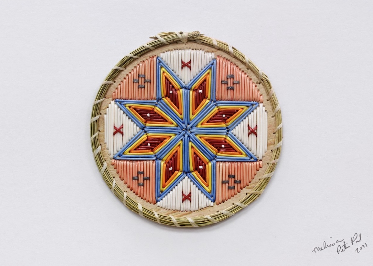 Each sections of an eight pointed star is made of red, yellow, orange and blue porcupine quills. Pink and white quills fill the remained of a circle on birchbark, within a woven exterior of sweetgrass.