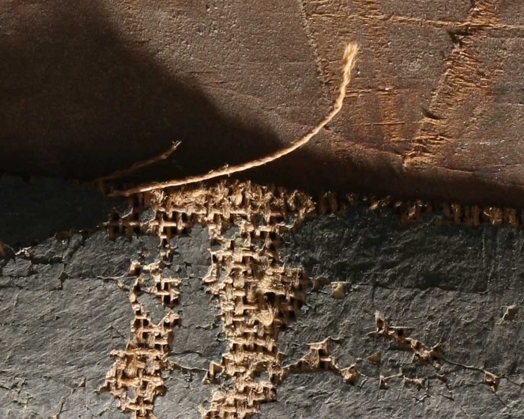 A damaged area of a painting exposes the fibres of the canvas below it.