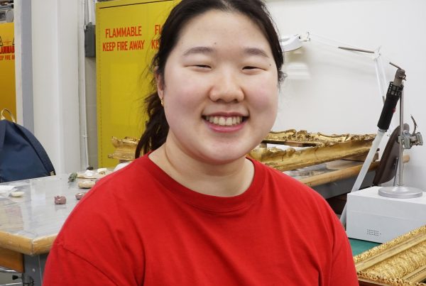 Shujung sits in the conservation lab, smiling. She is wearing a red t-shirt.
