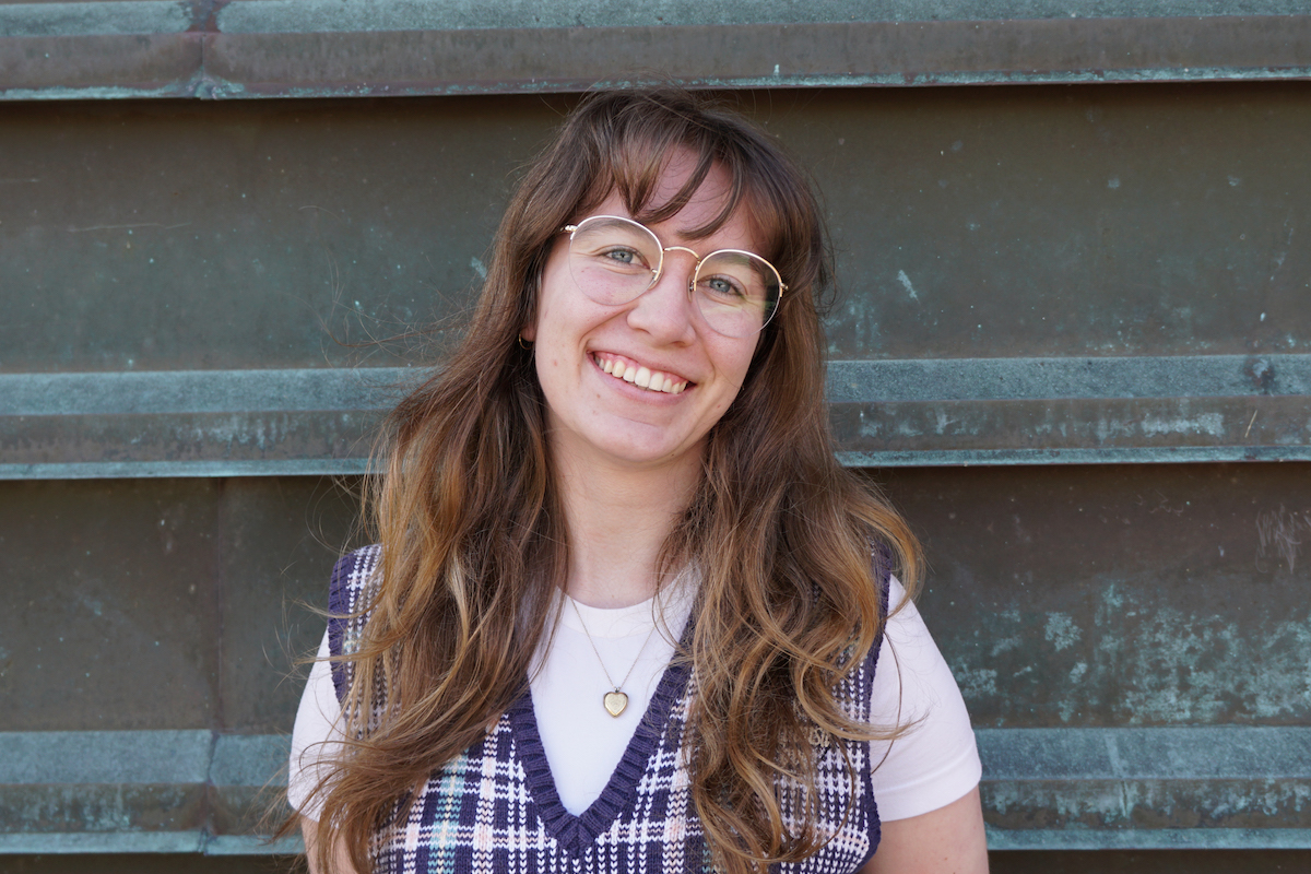 Dawn stands smiling in front of a textured metal background.