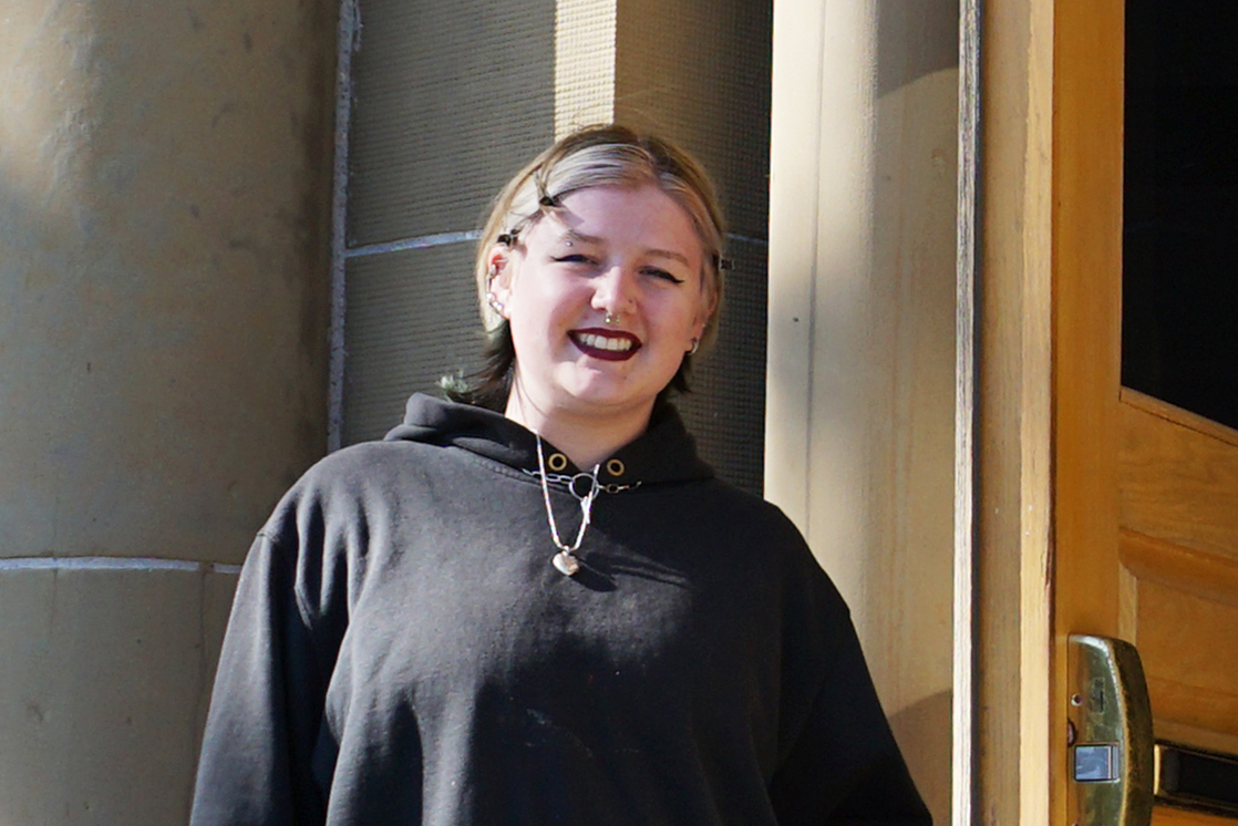 Jaden stands in front of the Owens Art Gallery, smiling.